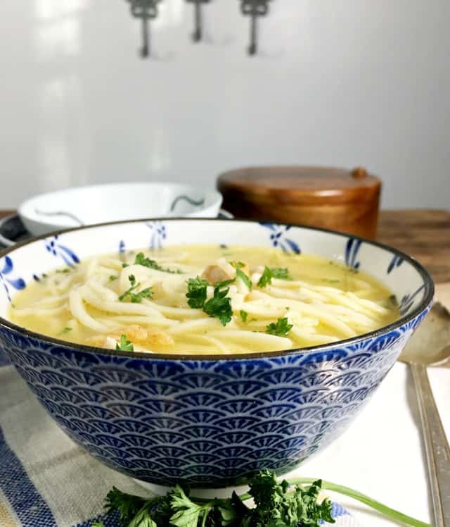 a blue bowl of soup on a blue and white napkin with round wooden box in back ground