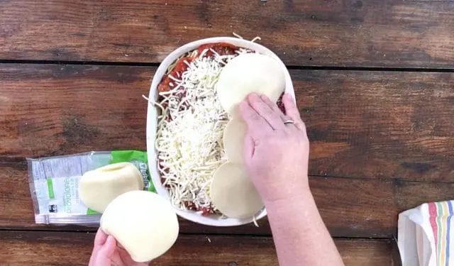 The second layer completed and now putting provolone on the top in a white bowl on brown table with sliced cheese beside