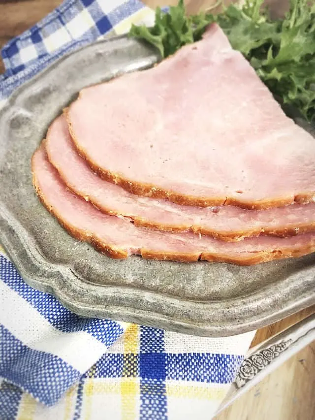 Three slices of ham on a gray plate with lettuce and a striped napkin