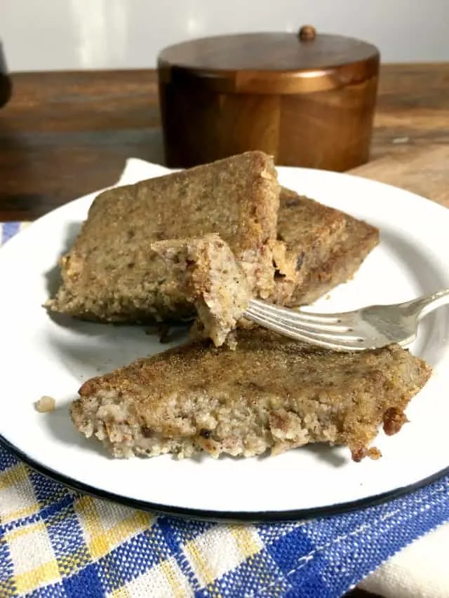 a white plate of scrapple with two slices on the plate and another part slice, fork holding piece