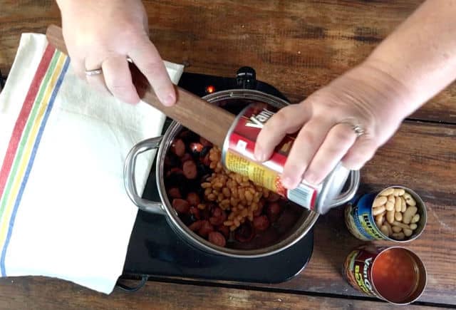 Adding a can of pork and beans to the saucepan