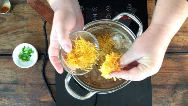 Adding the shredded cheddar cheese to the beans in the saucepan