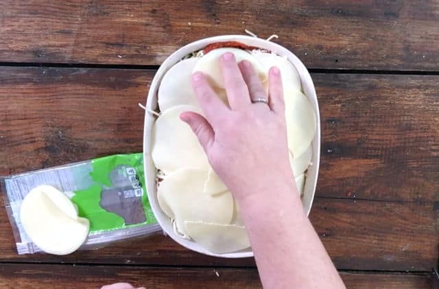 The final layer of spaghetti noodles, sauce and cheese in a white dish on a wooden back board