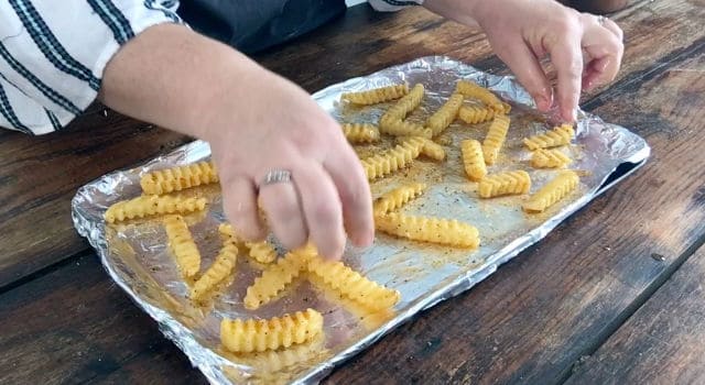 a baking sheet wrapped in aluminum foil with frozen fries, oil and seasoning on it