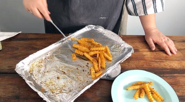 golden cooked fries being scooped off of baking sheet onto a blue plate