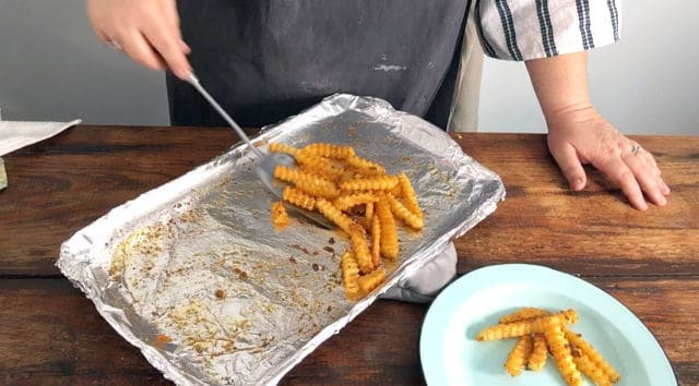 golden cooked french fries are scooped out of the baking tray onto a blue plate