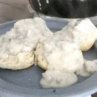 hamburger gravy covering two biscuits on a blue plate with skillet in background