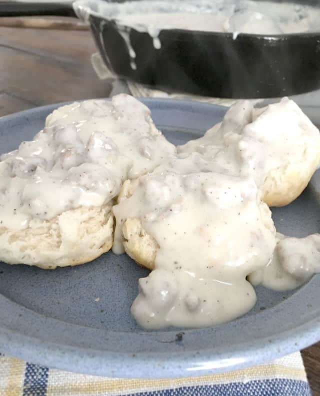 hamburger gravy covering two biscuits with steam rising up on a blue plate with skillet in background