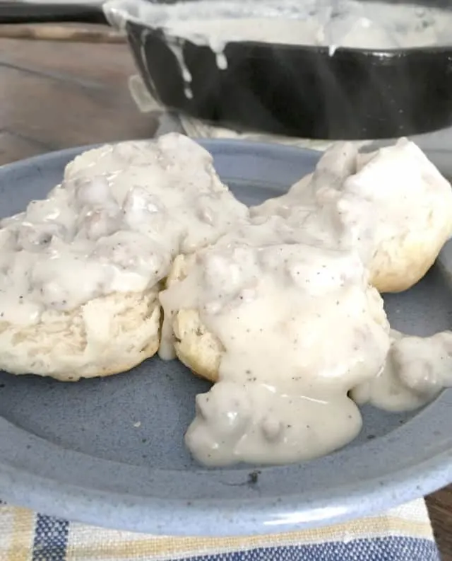 Blue plate with two biscuits covered in thick white sawmill gravy with lumps of sausage showing in the gravy.