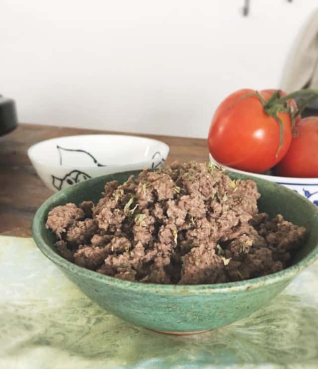 Side view of a green bowl holding ground beef sitting on a swirled green napkin 