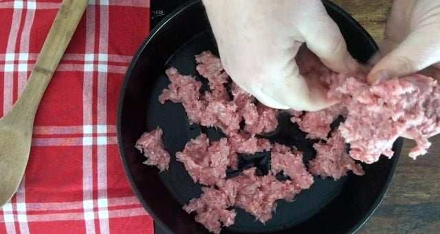 hand tearing up ground beef and putting in black skillet with red napkin