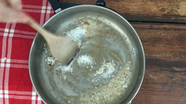 wooden spoon stirring flour into oil in a silver frying pan