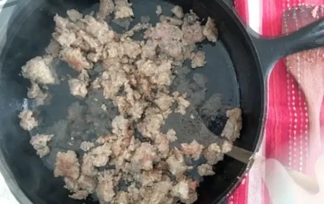Sausage in a black cast iron skillet being stirred and browned