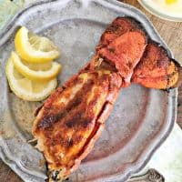 Red lobster tail with meat presented through the shell, lemon, gray plate