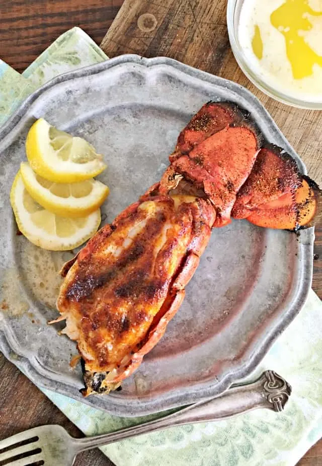 Red lobster tail with meat presented through the shell, lemon, gray plate