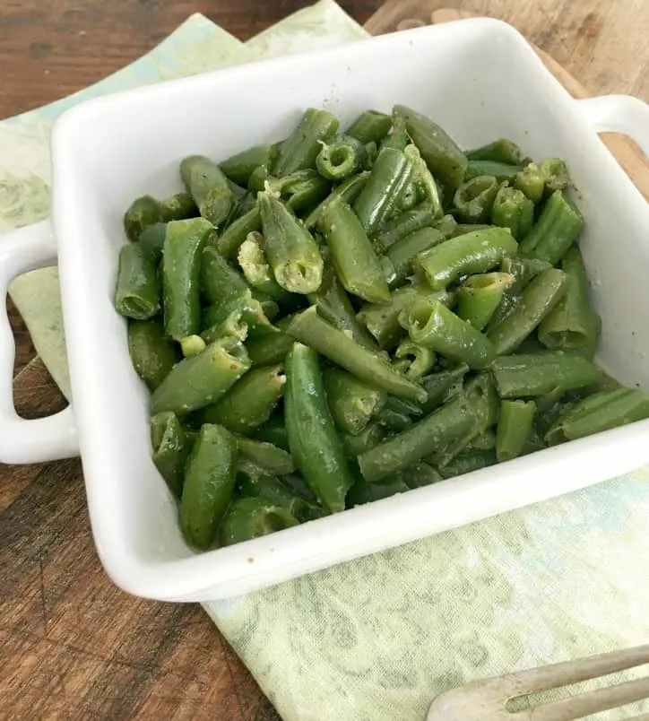 a small square white bowl holding the cooked green beans with green napkin underneath