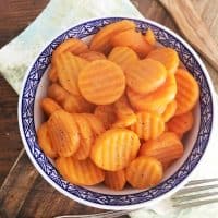 blue bowl of carrots with fork, green napkin and cutting board