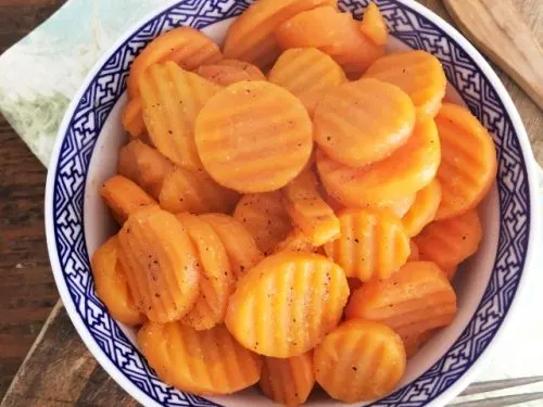 blue bowl of carrots with fork, green napkin and cutting board
