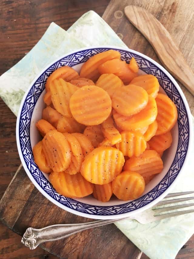 blue bowl of carrots with fork, green napkin and cutting board