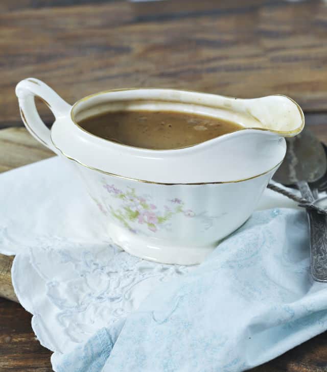 a china gravy boat filled with gravy sitting on a white napkin and wood table