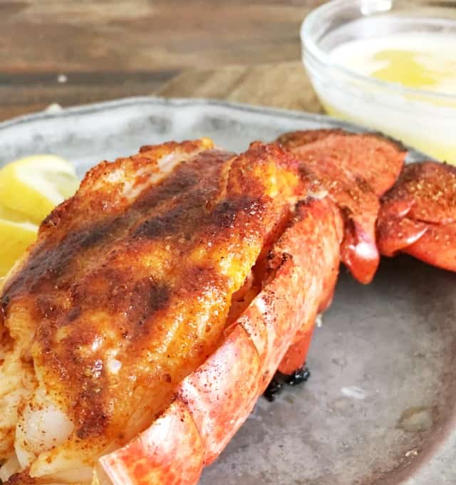 Close up of bright red lobster shell with meat presented, lemon and butter in back ground