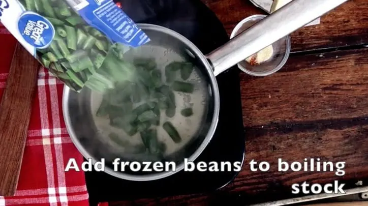 frozen green beans added to chicken stock in a saucepan