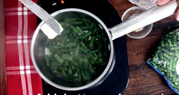 a pat of butter on a knife being added to saucepan of green beans