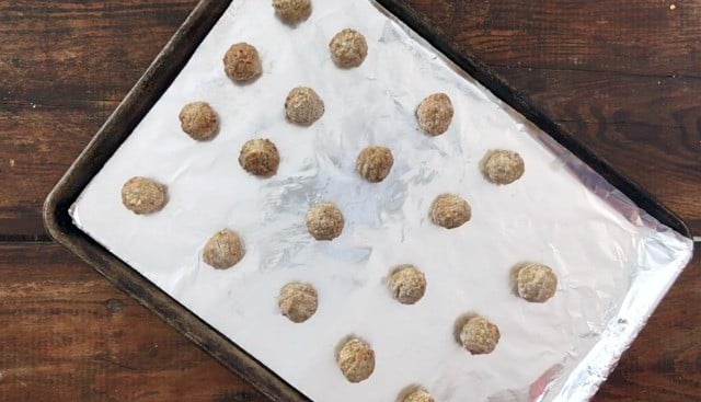 baking sheet covered in aluminum foil with frozen meatballs on it