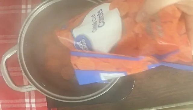 frozen carrots being poured into the boiling broth, silver pan with red napkin