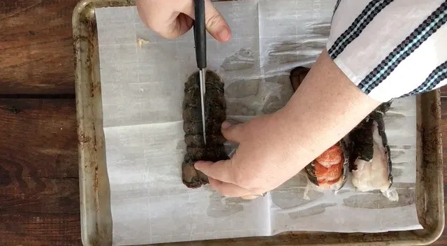 Hands using scissors to cut the lobster tail down the middle