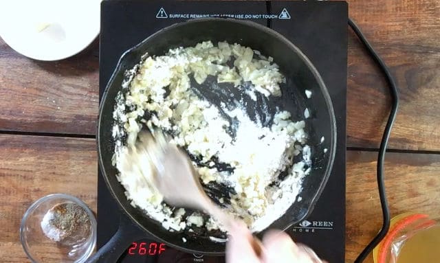 Frying pan with sauteed onions and flour added. Wooden spoon stirring