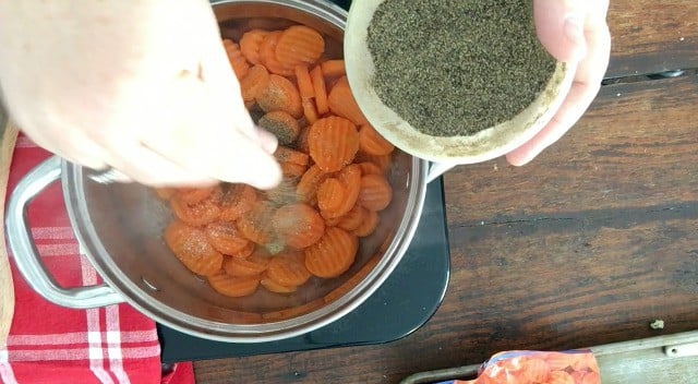hand sprinkling pepper on frozen carrots in stockpot