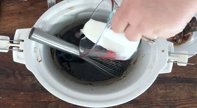 Hand pouring the glass fluid measure of cornstarch slurry into the crockpot of meat broth