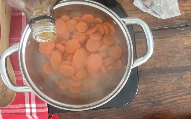 Maple syrup being poured into frozen carrots in silver pan, red napkin in background
