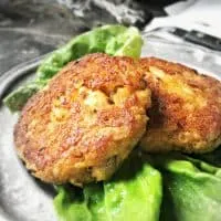 Two crab cakes on a silver plate with green lettuce.