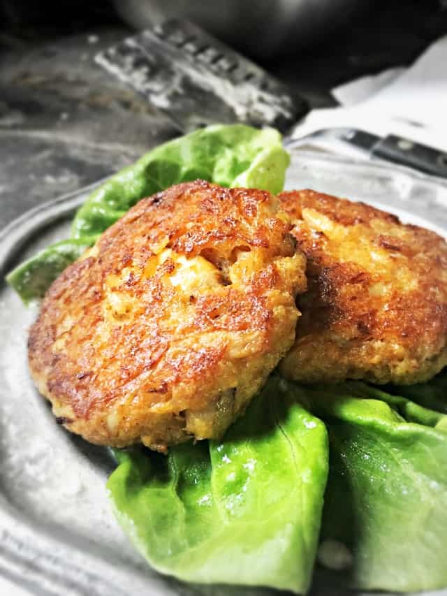Two crab cakes on a silver plate with green lettuce.