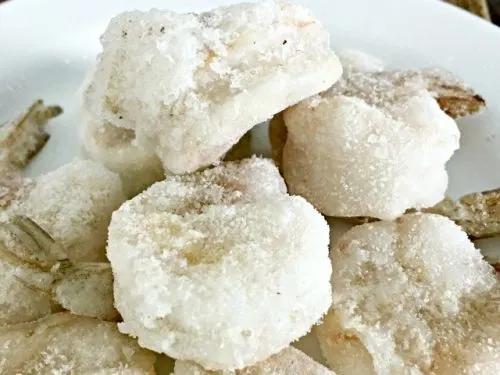 white plate with pile of frozen shrimp on top