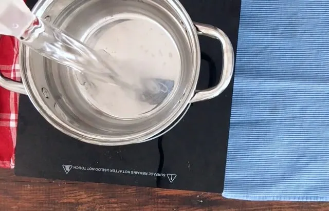 Water being poured into sauce pan on a cook top blue towel in back ground