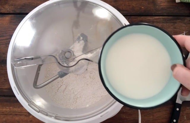 a blue bowl of milk held over the top of a stand mixer to be added