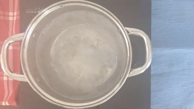 A saucepan on a cooktop with steam rising and bubbles from bottom