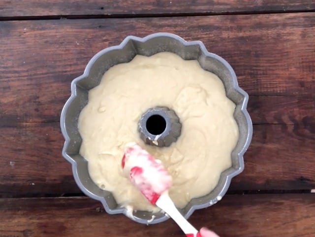 The batter for lemon pound cake recipe in a bundt pan with red spatula