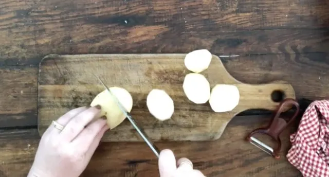 cutting board with hands slicing a potato