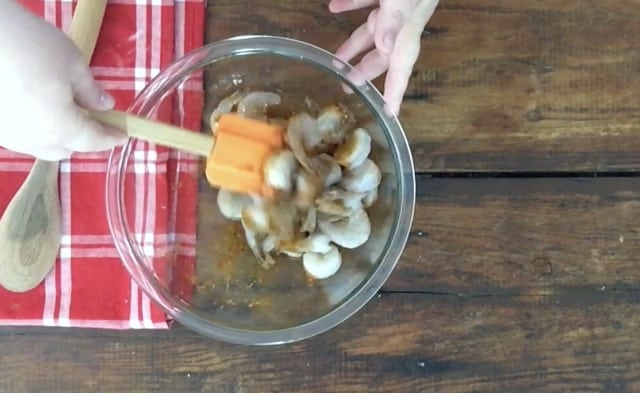 glass bowl, orange spatula mixing shrimp with oil and spices ready to put in the frying pan