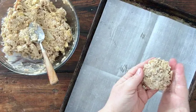 hands patting out crab patties with baking sheet and bowl in background