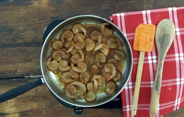 frying pan of seasoned frozen shrimp with red towel and orange spatular