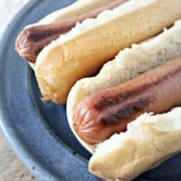 The ends of two hot dogs poking out from the edge of a bun on a blue plate