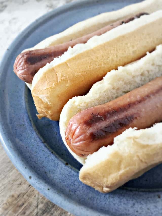 The ends of two hot dogs poking out from the edge of a bun on a blue plate