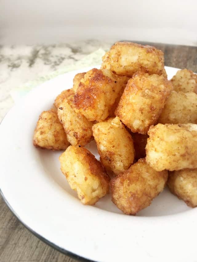 White plate with black rim on cutting board with tots