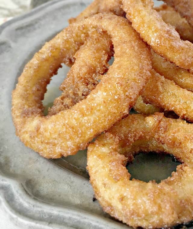 Close up for shiny onion rings on a grey plate sitting on a cutting board. 