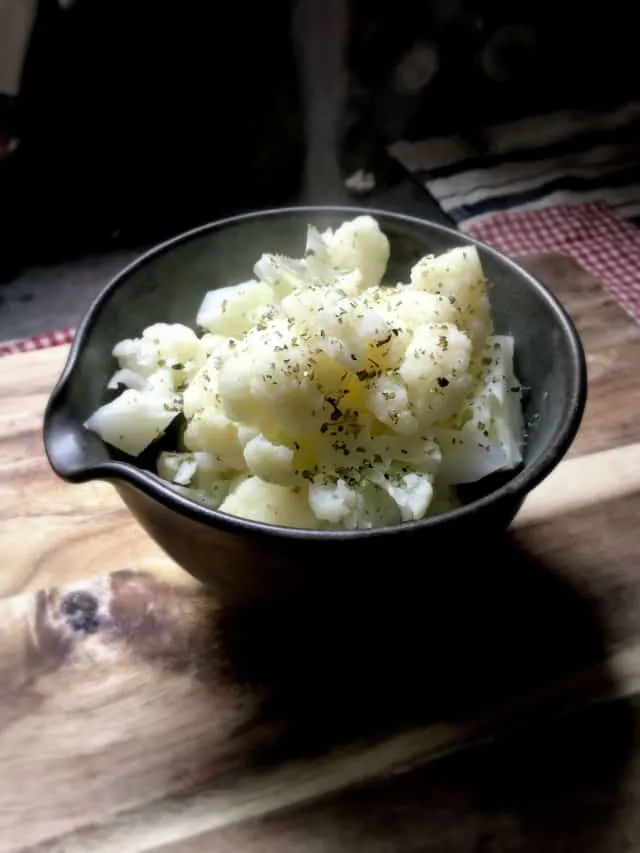 side view of a bowl of cauliflower with herbs sprinkled on top